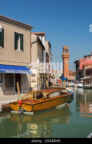 Vertäute Boote auf dem Kanal mit farbenfrohen Wohnhäusern, Häusern, Geschäften, Touristen und Uhrenturm auf dem San Stefano Platz, Murano Insel, Venedig Stockfoto