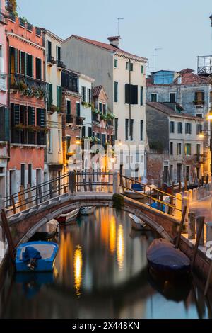 Vertäute Boote und Fußgängerbrücke über den Rio de la Toletta Kanal mit alten architektonischen Wohnhäusern in der Abenddämmerung, Dorsoduro Viertel, Venedig Stockfoto