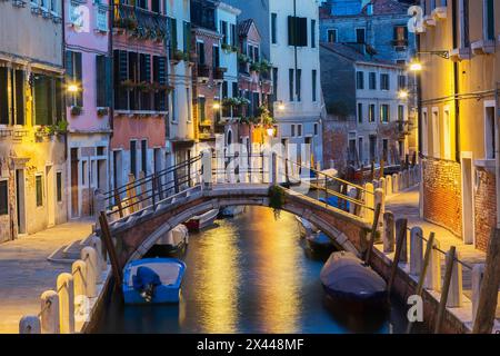 Vertäute Boote und Fußgängerbrücke über den Rio de la Toletta Kanal mit alten architektonischen Wohnhäusern in der Abenddämmerung, Dorsoduro Viertel, Venedig Stockfoto