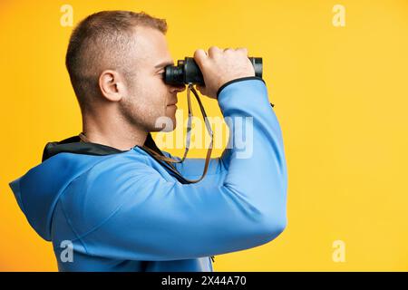 Junger Mann, der durch ein Fernglas schaut, isoliert auf gelbem Hintergrund. Seitenansicht Stockfoto