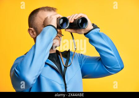 Junger Mann, der durch ein Fernglas schaut, isoliert auf gelbem Hintergrund. Seitenansicht Stockfoto