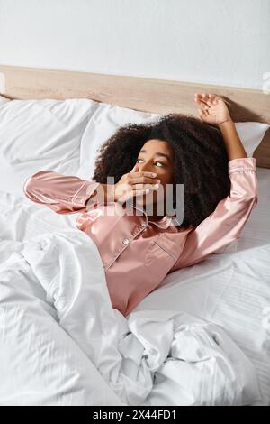 Eine lockige Afroamerikanerin im Pyjama liegt friedlich auf einem Bett, das mit weißen Laken bedeckt ist. Stockfoto