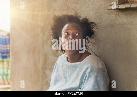 afrikanisches Dorf, einsame alleinstehende Frau vor dem Haus bei Sonnenuntergang, wartet auf der Veranda Stockfoto