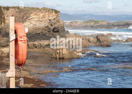 Ruhiger Strand mit Felsformationen, sanften Wellen, klarem Himmel und fernen Bergen, der Ruhe und natürliche Schönheit ausstrahlt Stockfoto