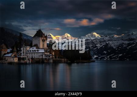 Schloss Oberhofen mit den Berner Alpen in der Winterdämmerung. Stockfoto