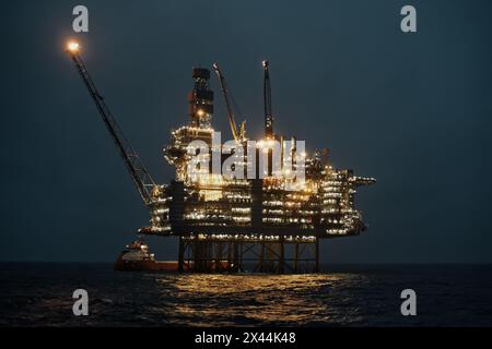 Offshore-Öl- und Gastankplattform, während des Frachtbetriebs mit Versorgungsschiffen in der Nacht im Meer. Stockfoto