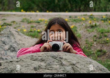 Porträt eines lächelnden Mädchens, das die Kamera hält, während er auf einem Felsen sitzt Stockfoto