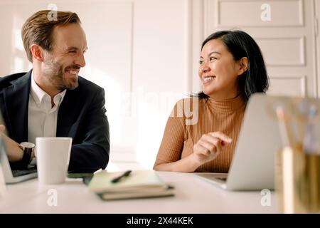 Glückliche Geschäftsfrau und Geschäftsmann sitzen mit Laptop im Büro Stockfoto