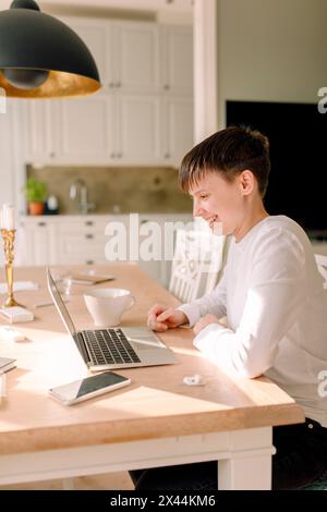 Lächelnde junge Geschäftsfrau mit Laptop, während sie am Esstisch in der Küche sitzt Stockfoto