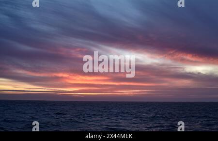 Farbenfroher Sonnenuntergang über dem Meer, mit lila und gelbem Himmel und ruhigem Wasser. Stockfoto