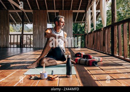 Reifer Mann, der Matsyendrasana auf Yogamatte im Wellnessresort spielt Stockfoto