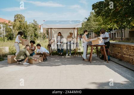 Multirassische Gruppe von Freiwilligen, die sich gegenseitig helfen, während sie sich auf eine Wohltätigkeitsaktion im Gemeindezentrum vorbereiten Stockfoto