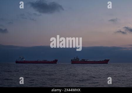 Silhouette von zwei Öltankern im Meer, früh am Morgen, mit blauem Himmel und ruhigem Wasser. Stockfoto