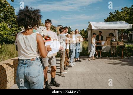 Team von männlichen und weiblichen Freiwilligen, die Spendengüter in Kisten überreichen, während sie während der Wohltätigkeitsfahrt in der Kommuni in Reihe stehen Stockfoto