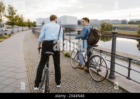 Männliche Geschäftsleute stehen mit Fahrrädern auf der Kopfsteinpflasterstraße an der Promenade Stockfoto