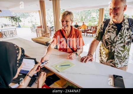 Glückliche ältere Frau, die den Zimmerschlüssel von der weiblichen Rezeptionistin an der Rezeption im Hotel nahm Stockfoto