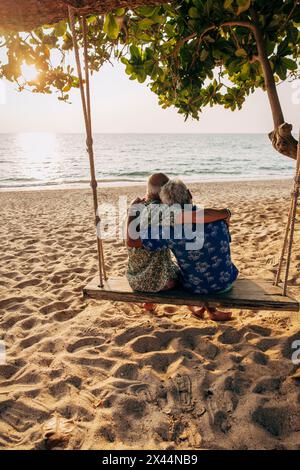 Romantisches schwules Paar, das auf einer Schaukel sitzt und auf den Strand blickt Stockfoto
