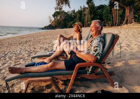 Glückliches älteres Paar, das auf Liegestuhl sitzt und den Urlaub am Strand genießt Stockfoto