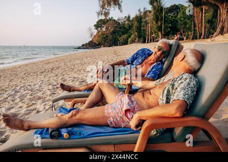 Glückliches älteres schwules Paar, das sich während des Urlaubs auf der Liege am Strand liegend Stockfoto