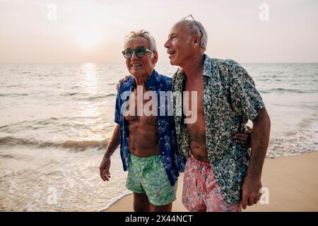 Sorgloses, schwules Seniorenpaar, das mit Armen in Strandnähe herumläuft Stockfoto