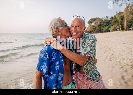 Ein älterer schwuler Mann küsst einen Freund im Urlaub am Strand Stockfoto