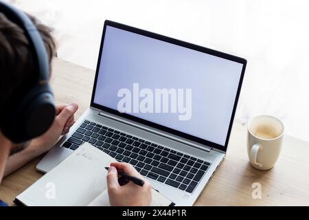 Kabellose Kopfhörer von man sitzen vor einem leeren weißen Bildschirm, an einem kleinen Tisch, machen Notizen in Notizbuch, Bilder in hellen Farben, Online-Unterricht oder Onlin Stockfoto