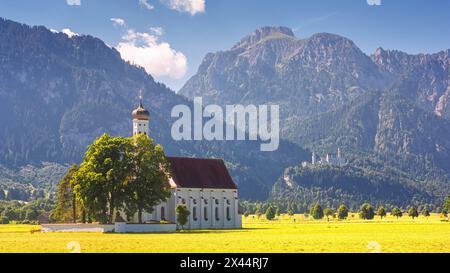 Bayerische Landschaft - Blick auf die Kirche St. Coloman im Hintergrund der Alpenberge und Schloss Neuschwanstein am Sommertag, Deutschland Stockfoto