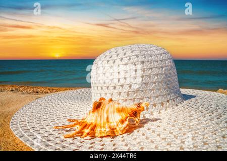 Nahaufnahme eines Sonnenhutes an einem Sandstrand am Meer bei Sonnenuntergang, selektiver Fokus. Strandurlaubskonzept, Hintergrund mit Kopierraum für Text Stockfoto