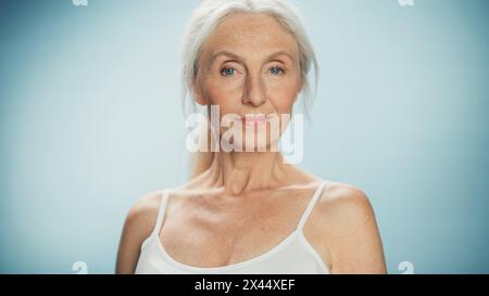 Porträt einer schönen Seniorin, die in die Kamera schaut und wundervoll lächelt. Ältere Dame mit natürlichen, üppigen grauen Haaren, blauen Augen, Top tragen. Schönheit und würde des Alters Stockfoto