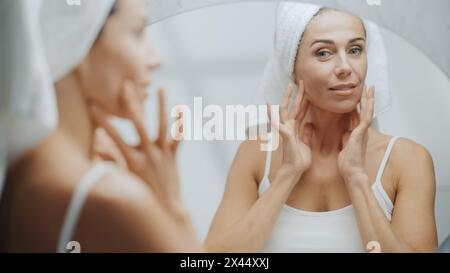 Schöne weiße Frau berührt ihre perfekte weiche Schulter, Hals, sinnlich sieht im Badezimmerspiegel aus. Frau Mittleren Alters Genießt Ihre Natürliche Schönheit Morning Routine. Überschulteraufnahme Stockfoto