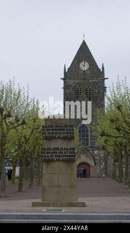 Sainte-Mere-Eglise, Frankreich - 19. April 2024: Kirche Sainte-Mere-Eglise. Leute, die in Sainte-Mere-Eglise laufen. Straßen und Gebäude. Lebensstil im Ur Stockfoto