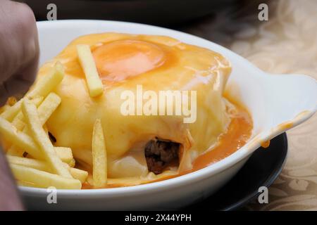 Das Francesinha, ein Sandwich aus Porto, Portugal, mit Schweinefleisch, geräucherter Wurst, Speck, Rindfleisch und einem Spiegelei, bedeckt mit einer käsigen Sauce Stockfoto