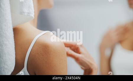 Schöne weiße Frau berührt ihre perfekte weiche Schulter, Hals, sinnlich sieht im Badezimmerspiegel aus. Happy Female genießt ihre natürliche Schönheit und Morning Routine. Nahaufnahme über Schulter Stockfoto