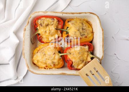 Köstliche gefüllte Paprika in der Auflaufform und Spachtel auf weißem, strukturiertem Tisch, Blick von oben Stockfoto