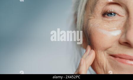 Close-up Porträt der schönen älteren Frau mit aufgetragener Augencreme. Ältere Dame macht ihre Haut weich, glatt, knitterfrei mit natürlicher Anti-Aging-Kosmetik. Produkt für Beauty Hautpflege Stockfoto