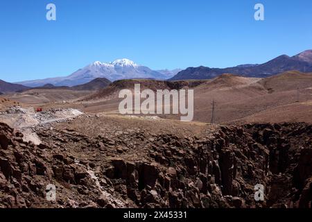 Blick auf die präkordilleren Wüstenhügel und den schneebedeckten Vulkan Nevados de Putre/Taapaca von der Nähe des Highway 11 in Copaquilla, Chile Stockfoto