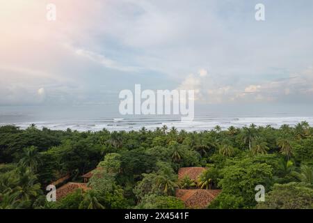 Hotelstil mit Meerblick. Rot gefliestes Villendach auf Palmenhintergrund neben Blick auf die Drohne am Strand Stockfoto