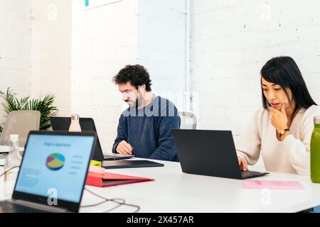 Gruppe von Menschen verschiedener Rassen, die konzentriert und glücklich mit Laptops in einem Coworking-Büro arbeiten Stockfoto