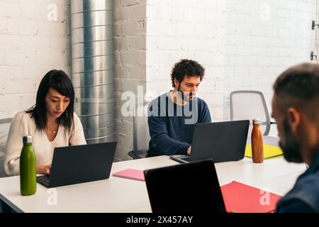 Gruppe von Menschen verschiedener Rassen, die konzentriert und glücklich mit Laptops in einem Coworking-Büro arbeiten Stockfoto