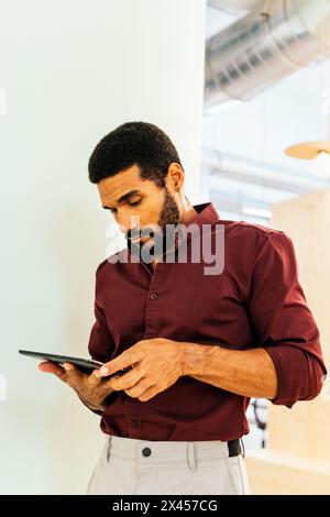 Hübscher lateinmann im Hemd, der mit einem Tablet in einem Coworking arbeitet Stockfoto