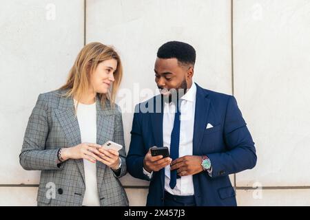 Geschäftsleute und Kollegen, die sich im Außenbereich unterhalten und ihr Smartphone nutzen. Sie tragen Anzüge und entspannen sich in einer Pause vor dem Büro Stockfoto