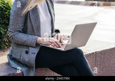 Nicht erkennbare Geschäftsfrau im Anzug, die draußen mit einem Laptop arbeitet Stockfoto