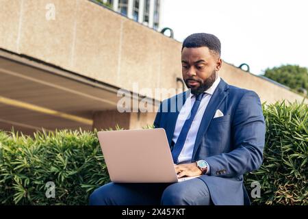 Schwarzer Geschäftsmann im Anzug, der draußen mit dem Laptop arbeitet Stockfoto