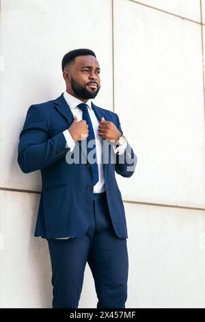 Porträt eines schwarzen Geschäftsmannes in einem Anzug, der seinen Blazer selbstbewusst anpasst Stockfoto