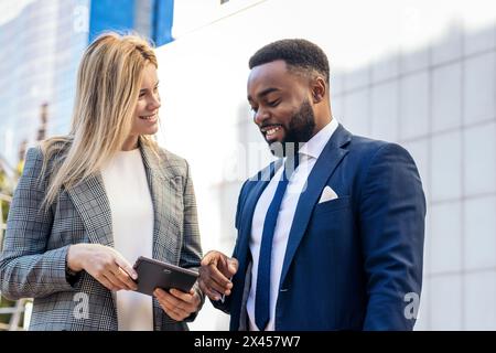 Geschäftsleute in Bürokleidung, die ein Tablet verwenden, um außerhalb des Büros über Unternehmensdaten zu sprechen Stockfoto