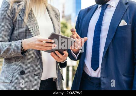 Geschäftsleute in Bürokleidung, die ein Tablet verwenden, um außerhalb des Büros über Unternehmensdaten zu sprechen Stockfoto