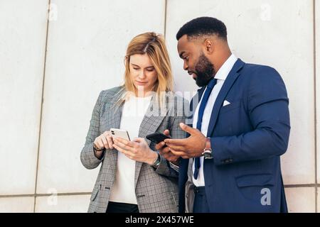 Geschäftsleute und Kollegen, die sich im Außenbereich unterhalten und ihr Smartphone nutzen. Sie tragen Anzüge und entspannen sich in einer Pause vor dem Büro Stockfoto