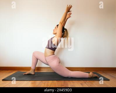 Junge mittelgroße Frau in einem rosa Sportoutfit, die zu Hause Yoga auf einer Matte macht. Stockfoto