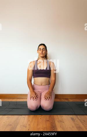 Junge mittelgroße Frau in einem rosa Sportoutfit, die zu Hause Yoga auf einer Matte macht. Stockfoto