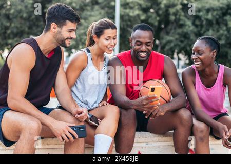 Gruppe multirassischer Freunde, die nach einem Basketballspiel ein Smartphone verwenden Stockfoto